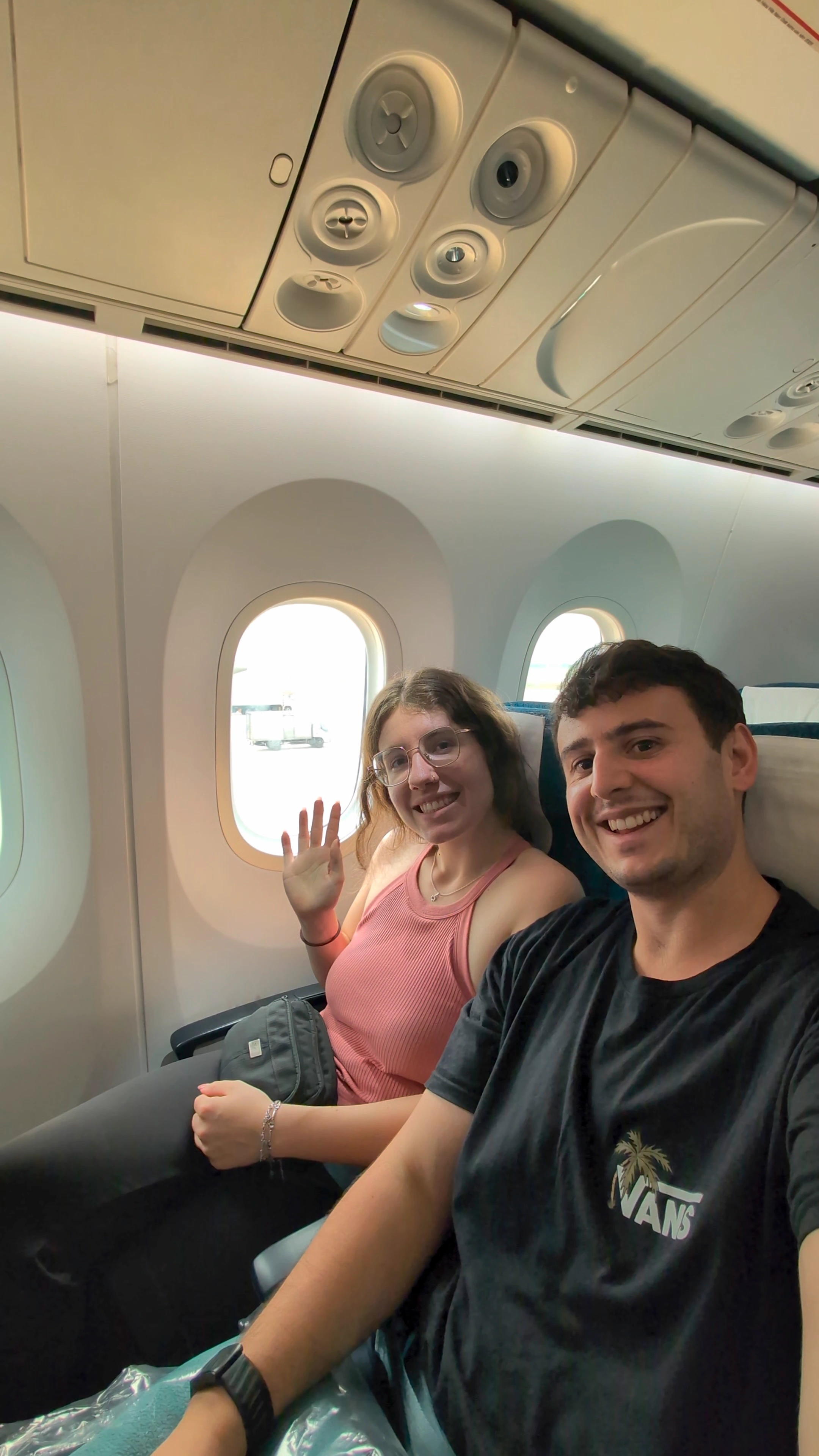 Liam and Sarah smiling and waving from their seats on a domestic flight in Vietnam